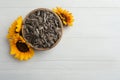 Raw sunflower seeds in bowl and flowers on white wooden table, top view. Space for text Royalty Free Stock Photo