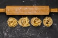 Raw tagliatelle with rolling pin for dough on black background