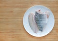 Raw tilapia fish fillet on white plate against wooden board background with copy space Royalty Free Stock Photo