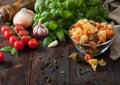 Raw tricolore trottole wheat pasta in glass bowl with oil and garlic, basil plant and tomatoes with pepper and linen towel on Royalty Free Stock Photo