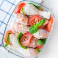 Raw uncooked chicken legs, drumsticks with tomatoes and basil in glass backing dish, square format, top view Royalty Free Stock Photo