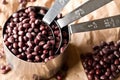 Raw, uncooked, dried adzuki red mung beans in metal measurement cups on brown packing paper background