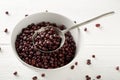 Raw, uncooked, dried adzuki red mung beans in white bowl with metal spoon on white wood table background