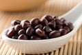 Raw, uncooked, dried adzuki red mung beans in white spoon on bamboo mat background