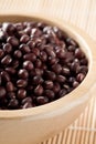 Raw, uncooked, dried adzuki red mung beans in wooden bowl on bamboo mat background