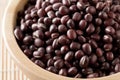 Raw, uncooked, dried adzuki red mung beans in wooden bowl on bamboo mat background