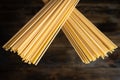 Raw uncooked Italian spaghetti , two stacks of pasta crossed over a dark wooden background
