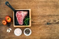 Raw uncooked meat t-bone steak with garlic, tomatoes, rosemary, salt and pepper in small dark cooking pan over rustic Royalty Free Stock Photo