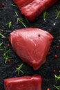 Raw venison steak with rosemary and pepper on black rustic table.