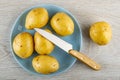 Raw washed potatoes, knife in plate, potato on wooden table. Top view