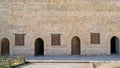 Raw of weathered wooden arched doors and closed rusted wrought iron windows on bricks stone wall