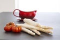 Raw white asparagus spears with pisanello tomatoes and a red gravy boat. Fresh vegetables on black table background Royalty Free Stock Photo