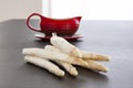 Raw white asparagus spears with a red gravy boat in background. Fresh vegetables on black table Royalty Free Stock Photo