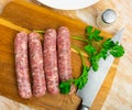 Raw white botifarra sausages on wooden board with knife and parsley