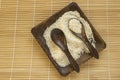 Raw white rice on a square wooden plate and two wooden spoons with rice on a bamboo napkin for healthy eating, vegetarianism, top