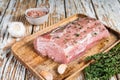 Raw Whole boneless pork loin meat with thyme and salt on rustic board. White wooden background. Top view