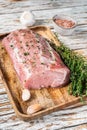 Raw Whole boneless pork loin meat with thyme and salt on rustic board. White wooden background. Top view