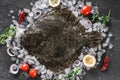 Raw whole flounder fish with spices on ice over dark stone background.