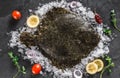 Raw whole flounder fish with spices and lemon on ice over dark stone background. Creative layout made of fish, top view