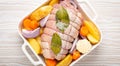 Raw wrapped rolled sliced pork in white casserole dish with potatoes, vegetables and herbs on rustic white wooden Royalty Free Stock Photo