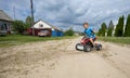 In the rays of the setting sun, a boy rides an ATV. Quad bike. A child rides along the road in a village on an ATV Royalty Free Stock Photo