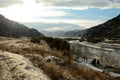 The rays of the setting sun through dense clouds illuminate a picturesque valley with a frozen riverbed in the snowy mountains on Royalty Free Stock Photo