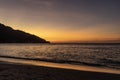 The rays of the sun setting behind the mountain paint the beach in a beautiful fiery color.