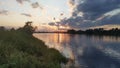 The rays of the sun setting over the river break through the clouds. Tall grass and trees grow along the river banks. The sun and Royalty Free Stock Photo