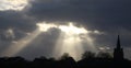 Rays of sunlight church spire tree top silhouettes