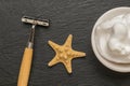 A razor with a wooden handle, a starfish and a bowl with shaving foam on a stone background. Flat lay