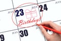 The hand circles the date on the calendar 23July, draws a gift box and writes the text Birthday. Holiday.