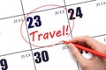 Hand drawing a red circle and writing the text TRAVEL on the calendar date 23July. Travel planning.