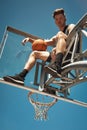 Reach for the sky or dont even try. Portrait of a sporty young man sitting on a basketball hoop on a sports court.