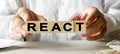 REACT inscription on the texture of wooden cubes. A business man holds a cube in his hand. An inscription on a financial, business