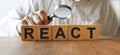 REACT inscription on the texture of wooden cubes. A business man holds a magnifying glass in his hand and examines the inscription