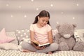 Read before sleep. Girl child sit bed with teddy bear read book. Kid prepare to go to bed. Pleasant time in cozy bedroom Royalty Free Stock Photo