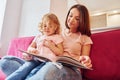 Reading big book. Young mother with her little daughter in casual clothes together indoors at home Royalty Free Stock Photo