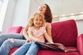 Reading big book. Young mother with her little daughter in casual clothes together indoors at home Royalty Free Stock Photo