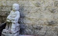 Reading book motion of Jizo little buddha statue sitting against old sandstone wall. Royalty Free Stock Photo