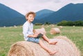 Reading boy sits over the haystack roll on the mountain field