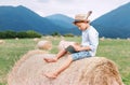 Reading boy sits over the haystack roll on the mountain field in