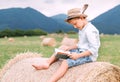 Reading boy sits over the haystack roll on the mountain field