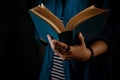 Reading Concept. Person Holding Opened Bible Book on Hand. Dark Tone