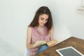 Reading, education, culture, people concept - young student woman is reading a book, while she is sitting on white chair