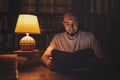 Reading and education. A man in the library reading a book in the evening by the light of a lamp. In the background, a rack of