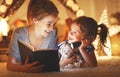 Mother and child daughter reading a book and a flashlight before Royalty Free Stock Photo