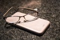 Reading glasses on top of a mobile phone on a marble table top Royalty Free Stock Photo