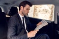 Reading latest news. Handsome young man in full suit reading a newspaper while sitting in the car