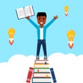 Young African American standing on pile of books holding an open book with a smile.