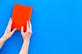 Reading for leasure. Hands take hardback book with empty cover on blue background top view space for text